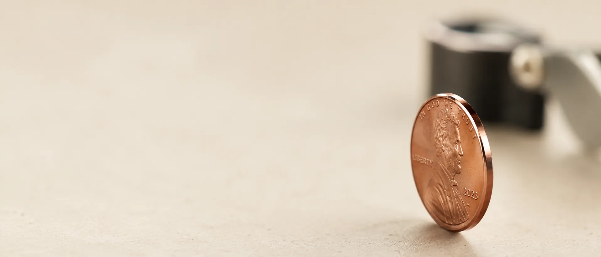 A cent standing on its edge beside an out-of-focus jeweler's loupe